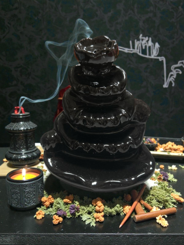 Fântâni Fum Pentru Conuri - Fântână de fum neagră din ceramică „Serendipity” cu fum curgător, așezată lângă o lumânare aprinsă și elemente naturale.