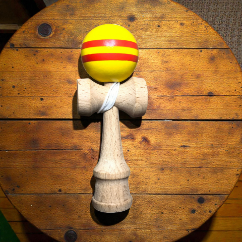 Kendame - Kendama mini de 12 cm din lemn natural cu bilă lucioasă dungată în culori galben și negru.