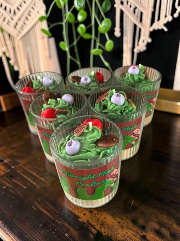 Delicii Parfumate: Lumânări Desert - Grup de șase lumânări artizanale în pahare de sticlă striată, cu design de desert stratificat Midnight Mint Praline, având topping din ceară verde sub formă de frișcă și decorațiuni de fructe și ciocolată.