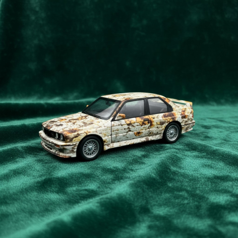 Mașini de colecție - Machetă metalică BMW M3 E30 scara 1:24 cu finisaj vopsea efect rugină pe fundal verde.