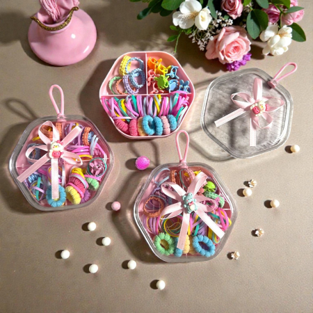 Clămițe colorate - Cutie octogonală cu capac transparent și fundiță roz, plină cu elastice de păr și clame colorate.