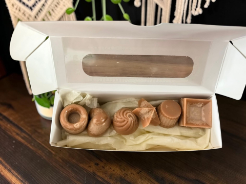 Delicii Parfumate: Lumânări Desert - Cutie albă deschisă ce conține șase pastile de ceară parfumată (wax melts) din ceară de soia, cu design hiper-realist de praline de ciocolată în diferite forme geometrice.